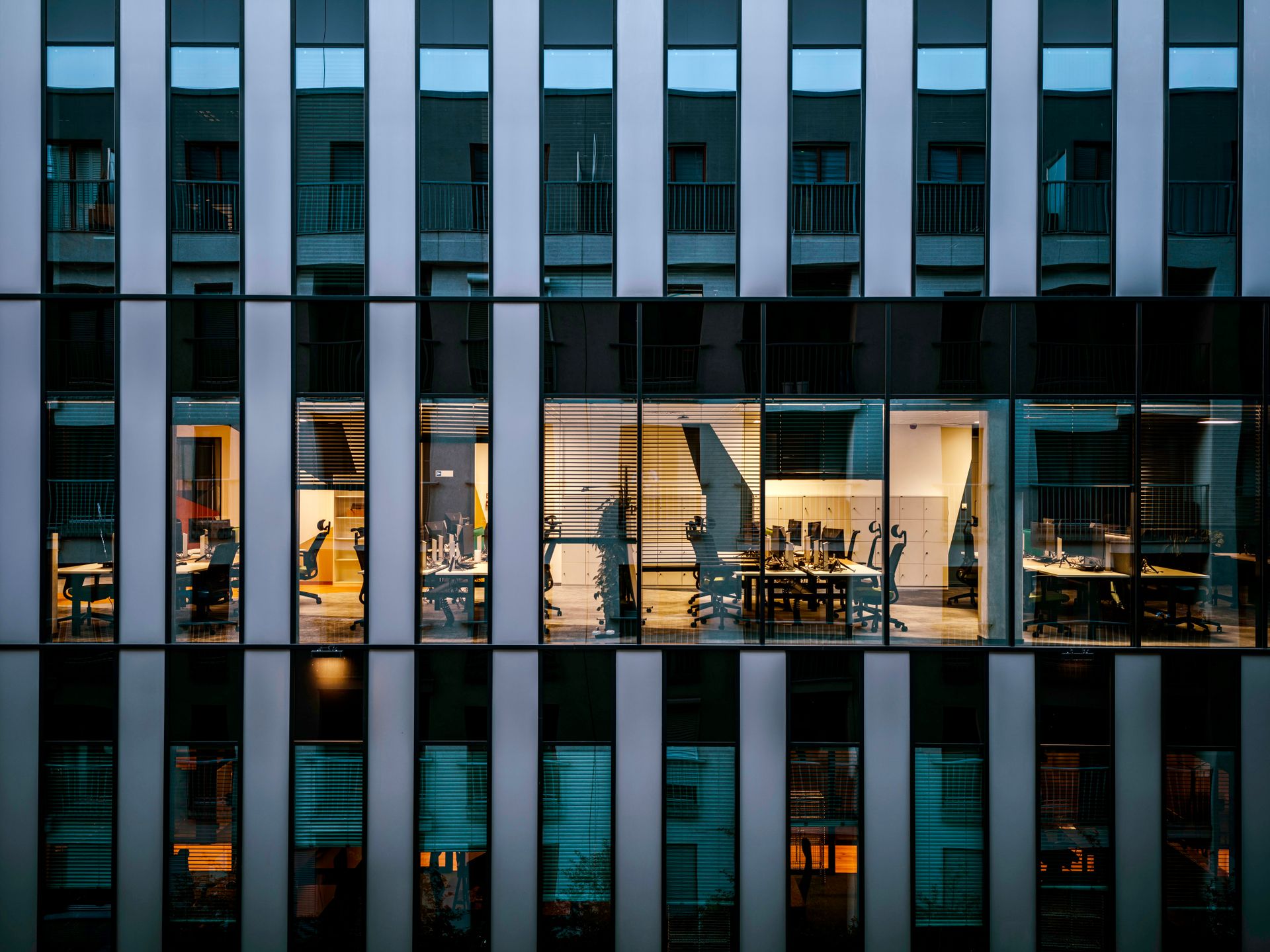 Corporate office façade at dusk with lit workspaces behind a glazed grid